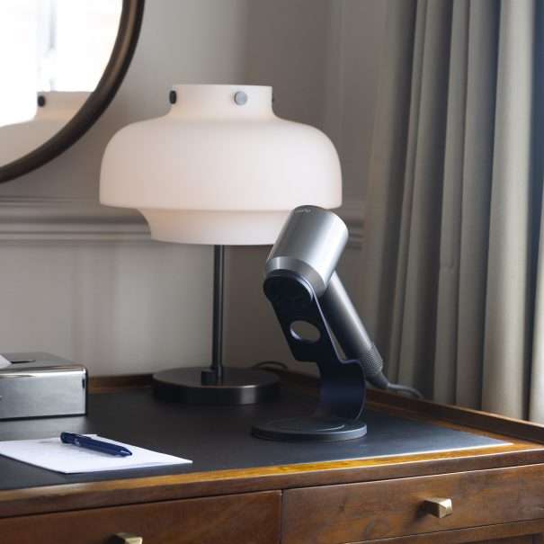 A wooden desk with a lamp, a modern microphone on a stand, a notepad, and a pen. A round mirror and curtain are in the background.