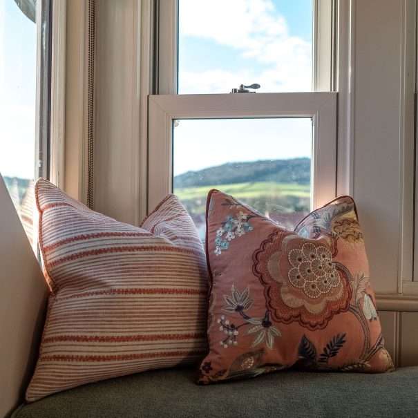 Zwei Zierkissen auf einer Fensterbank mit Blick auf sanfte Hügel und Häuser draußen.