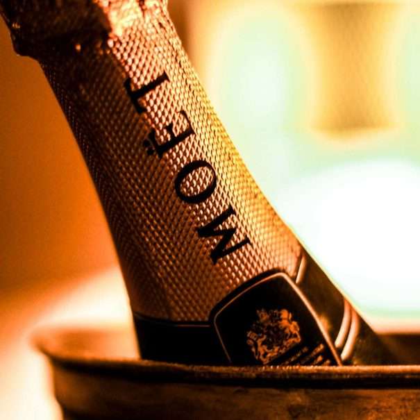 Gros plan d'une bouteille de champagne Moët dans un seau à glace en métal, sur un fond chaud et flou — parfait pour célébrer dans une retraite côtière.