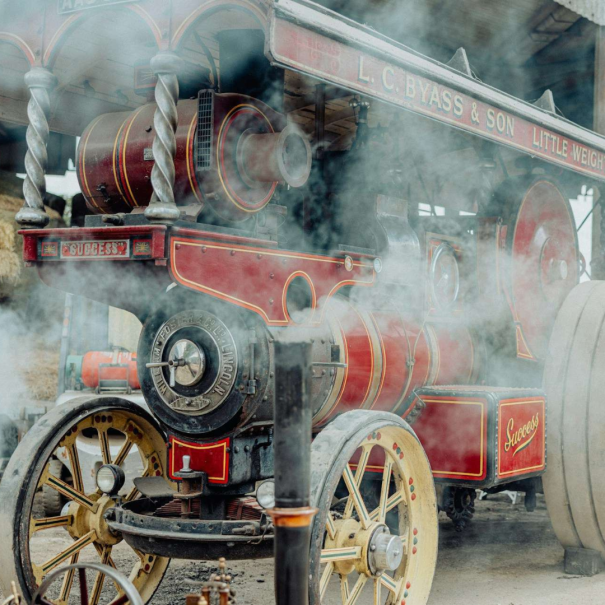 Eine historische Dampfzugmaschine mit roten und goldenen Details steht inmitten von Dampfwolken und zeigt den Namen 